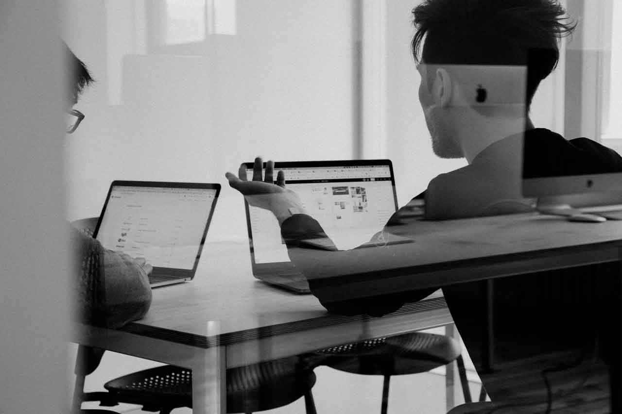 Two professionals discussing private company investment opportunities while working on laptops.